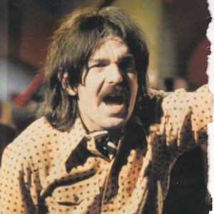May include: A man with long brown hair and a mustache is wearing a yellow and brown polka dot shirt. He is singing and has his mouth open. The caption below the image reads "Captain Beefheart: going completely polka-dotty."