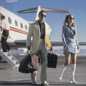 Może przedstawiać: Mężczyzna w kremowym garniturze i kobieta w niebieskim stroju idą po płycie lotniska w pobliżu prywatnego odrzutowca. Mężczyzna niesie dużą brązową torbę i czarną teczkę. Kobieta ma na sobie białe buty. Tekst na zdjęciu mówi "Las Vegas jest miejscem drugich szans."