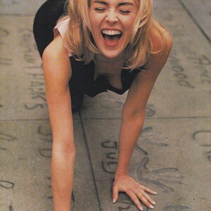 Może przedstawiać: Kobieta z blond włosami śmieje się, będąc na czworakach na betonowej powierzchni. Powierzchnia ma kilka odcisków dłoni.