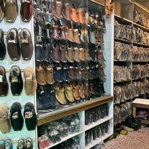 May include: A shoe store display featuring a variety of leather shoes in shades of brown, black, and tan. The shoes are displayed on shelves and in a glass cabinet, showcasing different styles of footwear.