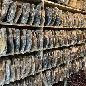 May include: Shelves filled with wrapped leather shoes in various colors, including black, brown, and tan. The shoes are neatly arranged and packaged in clear plastic, suggesting a retail setting or storage area.