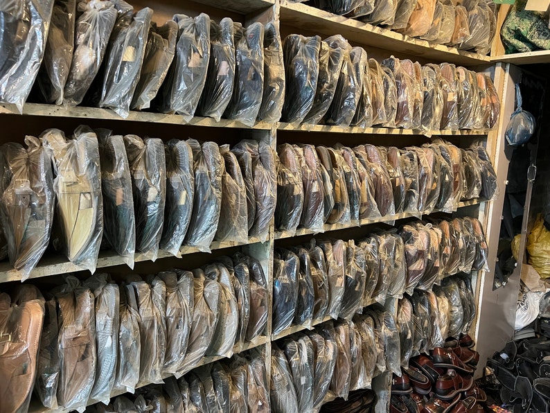 May include: Shelves filled with wrapped leather shoes in various colors, including black, brown, and tan. The shoes are neatly arranged and packaged in clear plastic, suggesting a retail setting or storage area.