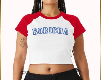 May include: A white cropped t-shirt with red sleeves and the word "BORICUA" in blue lettering. The shirt has a relaxed fit and a slightly cropped hem.