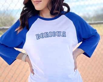 Puede incluir: Una camiseta de béisbol blanca y azul real con la palabra "BORICUA" en letras azules delineadas en la parte delantera.