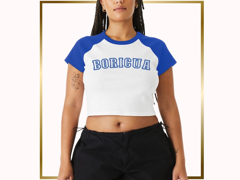 Puede incluir: Camiseta blanca y azul recortada con un dise&ntilde;o de estilo b&eacute;isbol. La camiseta tiene un dise&ntilde;o de bloque de color azul y blanco y dice "BORICUA" en letras azules.