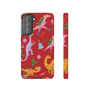 Può includere: Una custodia per telefono rossa con un motivo di dinosauro natalizio. I dinosauri indossano luci di Natale e cappelli. La custodia ha un ritaglio per l'obiettivo della fotocamera.