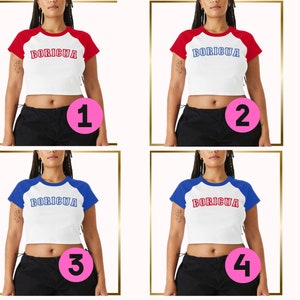 Puede incluir: Cuatro crop tops blancos con mangas de color rojo y azul. Las tops tienen la palabra "BORICUA" impresa en letras rojas y azules en la parte delantera. Cada top est&aacute; numerado del 1 al 4.
