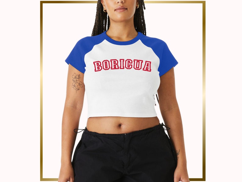 Puede incluir: Una camiseta blanca recortada con mangas ragl&aacute;n azules y la palabra "BORICUA" impresa en rojo en la parte delantera.