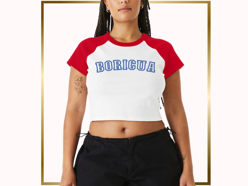 Puede incluir: Una camiseta blanca recortada con mangas rojas y la palabra "BORICUA" en letras azules. La camiseta tiene un corte holgado y un dobladillo ligeramente recortado.
