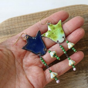 Puede incluir: Pendientes hechos a mano con colgantes de esmalte en forma de estrella en azul y verde. Los pendientes tienen ganchos dorados y est&aacute;n adornados con cuentas verdes y peque&ntilde;os abalorios con forma de flor. Un accesorio &uacute;nico.