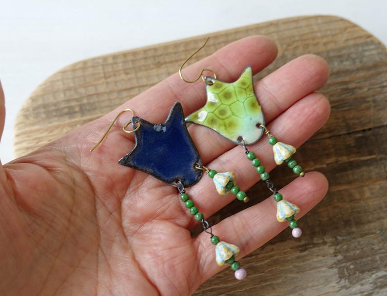 Puede incluir: Pendientes hechos a mano con colgantes de esmalte en forma de estrella en azul y verde. Los pendientes tienen ganchos dorados y est&aacute;n adornados con cuentas verdes y peque&ntilde;os abalorios con forma de flor. Un accesorio &uacute;nico.