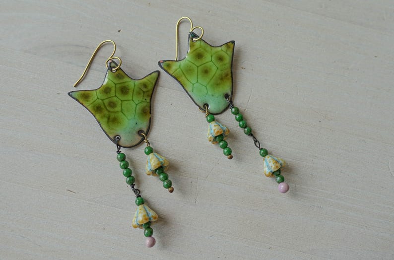 Puede incluir: Un par de pendientes hechos a mano con un dise&ntilde;o verde en forma de hoja y un patr&oacute;n texturizado. Los pendientes tienen ganchos dorados y cadenas colgantes con cuentas verdes, peque&ntilde;as flores amarillas y azules y una cuenta rosa al final.