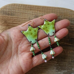 Puede incluir: Pendientes de esmalte verde y amarillo hechos a mano con una forma org&aacute;nica &uacute;nica. Los pendientes presentan un patr&oacute;n texturizado y cuelgan con cuentas verdes y peque&ntilde;os detalles florales. Los ganchos para las orejas de color dorado completan el dise&ntilde;o.