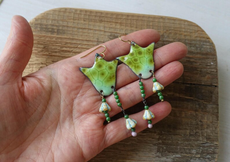 Puede incluir: Pendientes de esmalte verde y amarillo hechos a mano con una forma org&aacute;nica &uacute;nica. Los pendientes presentan un patr&oacute;n texturizado y cuelgan con cuentas verdes y peque&ntilde;os detalles florales. Los ganchos para las orejas de color dorado completan el dise&ntilde;o.