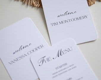 May include: White, rounded-corner cards with black text. One card reads "welcome" and "TIM MONTGOMERY." Another reads "welcome" and "VANESSA COOPER." A third card says "The Menu" with menu items listed below.