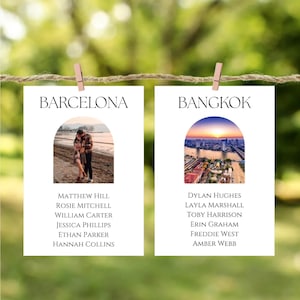 May include: Two white cards suspended by wooden pegs on a string, featuring the words "BARCELONA" and "BANGKOK". Each card displays a photograph and guest names. The Barcelona card shows a couple, and the Bangkok card shows a cityscape at sunset.