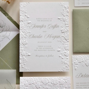 Può includere: Un invito di nozze bianco con motivi floreali di rose in rilievo lungo i bordi sinistro e destro. Il testo recita: Kindly join us at the wedding of Jennifer Griffin and Charlie Morgan, 20 August 2028, three o'clock in the afternoon, the Maya Bay, Florida, reception to follow.