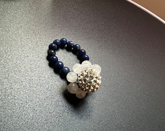 Puede incluir: Un brazalete de cuentas azules y blancas con una pieza central de diamantes de imitación plateados.
