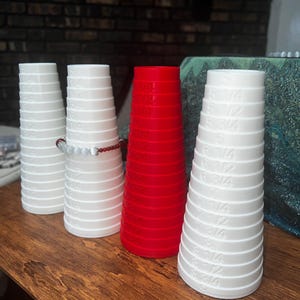 May include: Four ring sizers, three white and one red, with size markings in fractions of an inch. The sizers are stacked on a wooden surface.