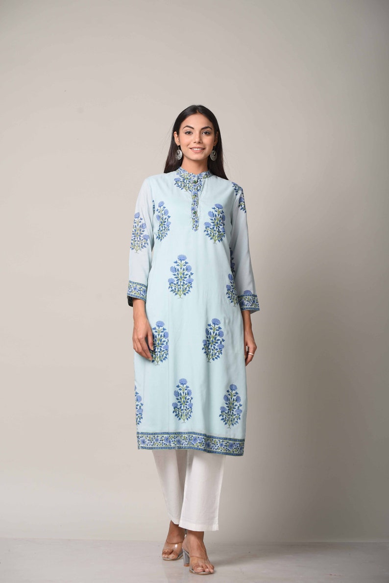 May include: A light blue long-sleeved kurta with a floral print in shades of blue and green. The kurta has a mandarin collar and a button closure. The model is wearing white pants and is standing against a white background.