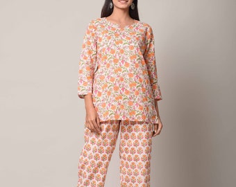 Op de afbeelding: Een witte katoenen pyjamaset met een bloemenprint in tinten oranje, roze en groen. Het bovenstuk heeft een V-hals en driekwart mouwen. De broek is recht.