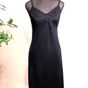 May include: A black slip dress with delicate lace trim at the hem and neckline. The dress features thin spaghetti straps and a V-neckline. The slip is displayed on a mannequin.