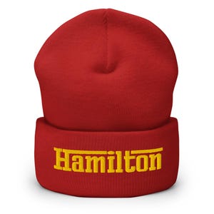 Puede incluir: Gorro rojo con un logotipo "Hamilton" bordado en amarillo.