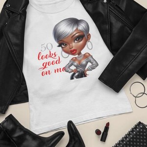 May include: White t-shirt with a cartoon illustration of a woman with silver hair and the text "50 looks good on me" in red script. The image also includes a black leather jacket, black boots, sunglasses, and a studded purse.