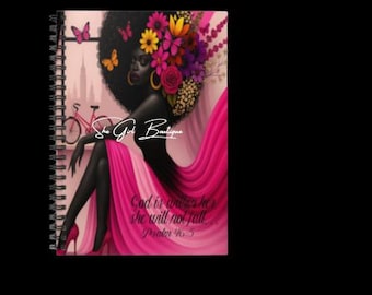 May include: Spiral-bound notebook featuring an illustration of a Black woman with floral hair and a pink dress. The notebook has the text "She Girl Boutique" and "God is within her, she will not fall. Psalm 46:5".