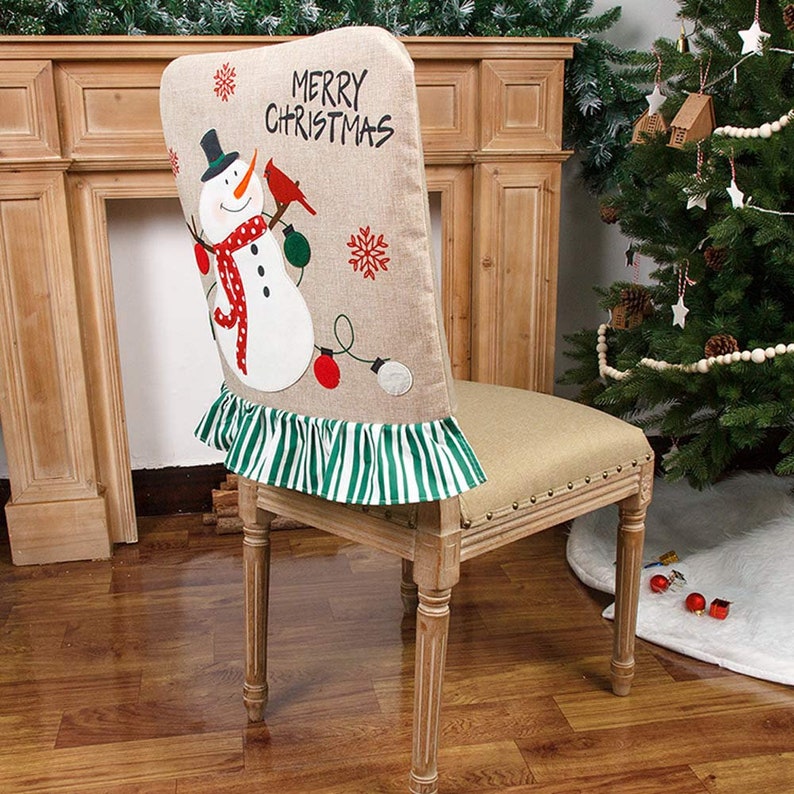 May include: A beige chair back cover with a snowman and robin applique. The cover has a green and white striped ruffle and the text "Merry Christmas".