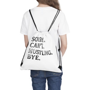 Puede incluir: Bolsa de cordón blanca con texto negro que dice "SORRY. CAN'T. HUSTLING. BYE."
