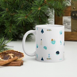 May include: White ceramic mug with a blue and white pattern of winter and ocean-themed illustrations. The pattern includes a snowman, seashells, a lighthouse, a Christmas tree, a seahorse, and a cup of hot chocolate.