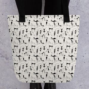 May include: A white tote bag with black handles and a repeating pattern of black cats in various poses. The cats are stylised and have long, thin tails.
