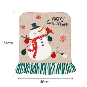 May include: A beige Christmas chair cover featuring a snowman and cardinal design. The cover has a green and white striped ruffle and reads "Merry Christmas". It measures 46cm wide and 54cm tall.