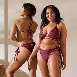 Pode incluir: Conjunto de biqu&iacute;ni bord&ocirc; com estampa de morcegos. O traje de banho de duas pe&ccedil;as apresenta um top triangular e calcinha com la&ccedil;os laterais. O tecido vermelho escuro &eacute; estampado com silhuetas de morcegos pretos. O biqu&iacute;ni &eacute; usado por duas pessoas.