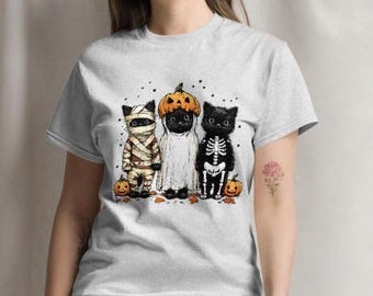Pode incluir: T-shirt cinza claro com um gráfico temático de Halloween. O gráfico mostra três gatos pretos vestidos de múmia, fantasma e esqueleto, com abóboras e folhas. Os gatos estão em fila.