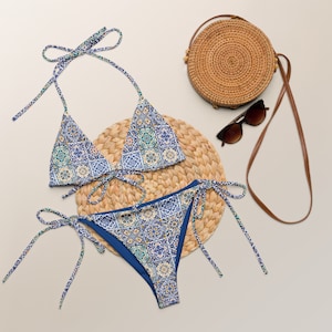 Może przedstawiać: Niebieski i biały wzorzysty bikini z dopasowaną słomianą torebką i okularami przeciwsłonecznymi. Górna część bikini to trójkątny styl z regulowanymi ramiączkami, a dolna część to wysoki krój z wiązaniami po bokach.