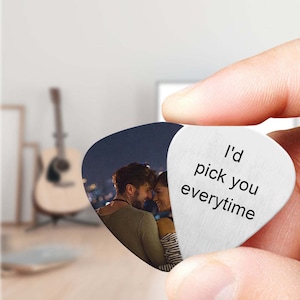 Op de afbeelding: Een zilveren gitaarplectrum met een foto van een stel op de ene kant en de tekst "I'd pick you everytime" op de andere kant.