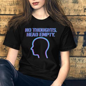 Pode incluir: Camiseta preta com o texto "NO THOUGHTS. HEAD EMPTY." em gradiente azul e roxo. Abaixo, um perfil de cabeça em azul e roxo.