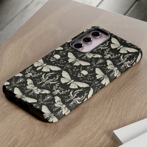 May include: A black phone case with a white and black pattern of moths, skulls, and flowers. The case has a camera cutout with three lenses.