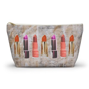 May include: A beige zippered pouch with a vintage newspaper print design. The pouch features a row of seven lipstick tubes with various shades of red, pink, and orange.