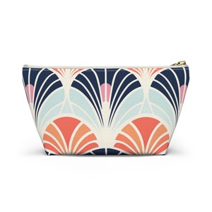 May include: A white zippered pouch with a geometric pattern in shades of blue, pink, orange, and white. The pattern features a repeating design of overlapping fan shapes.