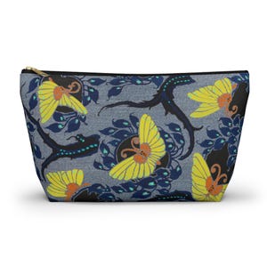 May include: A zippered pouch with a floral and lizard pattern. The design features yellow flowers with orange centers, dark blue leaves, and black lizard-like figures on a gray background. The zipper is gold-colored.