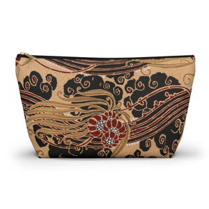 May include: A beige zippered pouch with a black and gold floral pattern. The pattern features red flowers and swirling lines.