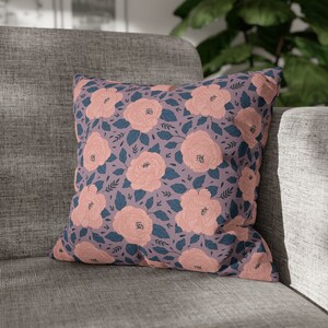 May include: A pink and blue floral patterned throw pillow with a soft, textured fabric. The pillow is sitting on a gray couch.