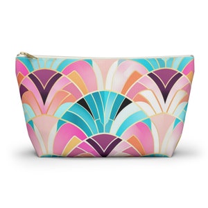 May include: A pink, blue, and gold geometric patterned zippered pouch. The pattern is made up of overlapping semi-circles.