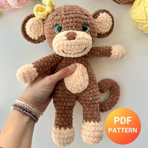May include: A crocheted monkey toy in brown and cream colours, with a yellow bow. The monkey has green eyes and is being held. The image includes the text "EASY" and "PDF PATTERN".