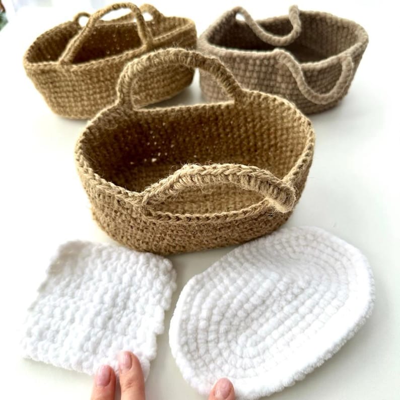 May include: Four handmade jute baskets with handles in varying shades of brown. Two white, fluffy, crocheted pads are in the foreground. The baskets are round and have a woven texture, perfect for storage or decor.