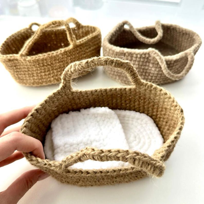 May include: Three small, hand-woven jute baskets with handles. One basket contains a white, fluffy item. The baskets are a natural tan color and appear to be handmade. The baskets are ideal for storage or decoration.