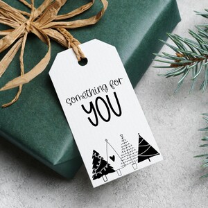 May include: A wrapped gift with a white tag that reads "something for YOU" in black script. The tag features three illustrated Christmas trees. The gift is wrapped in dark green paper and tied with a brown raffia bow.